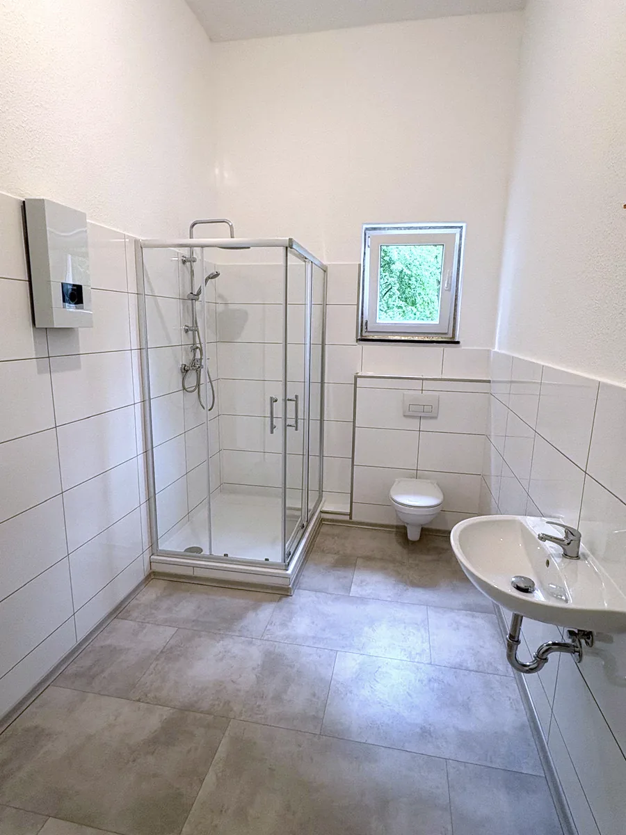 Badezimmer nach der Sanierung: neue Dusche, WC, Waschbecken und Fliesen